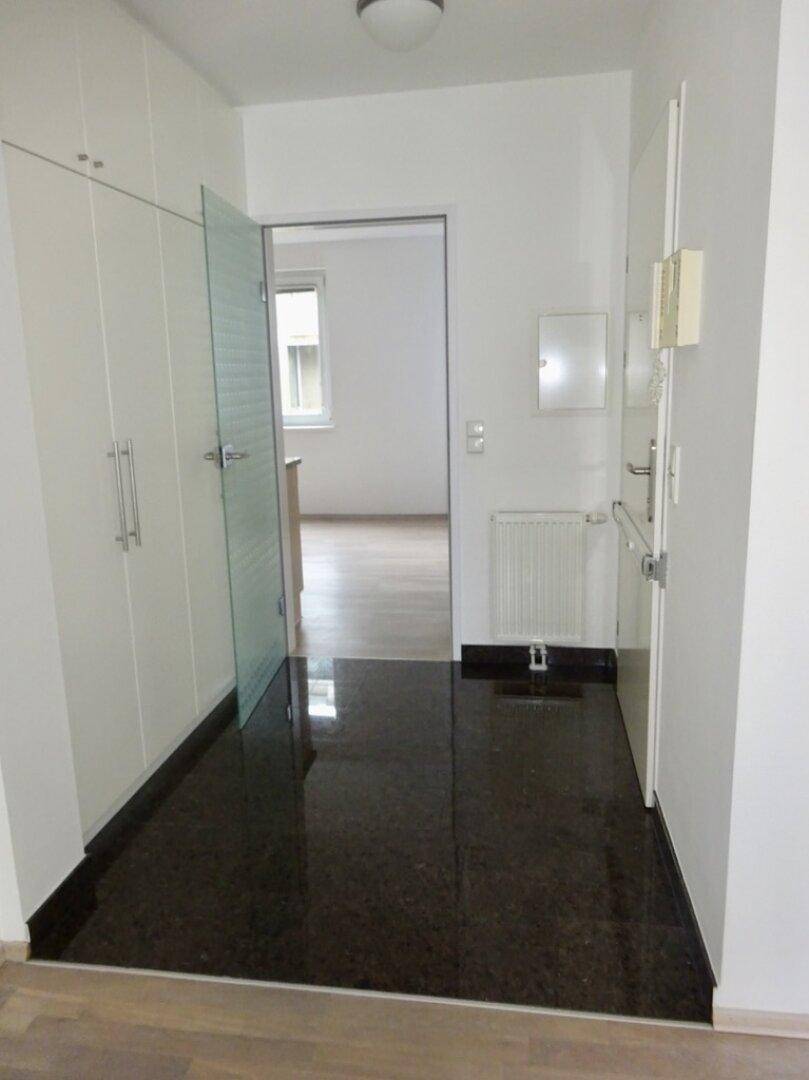 Heller Eingangsbereich mit dunklem Granitboden und integrierten Schränken.