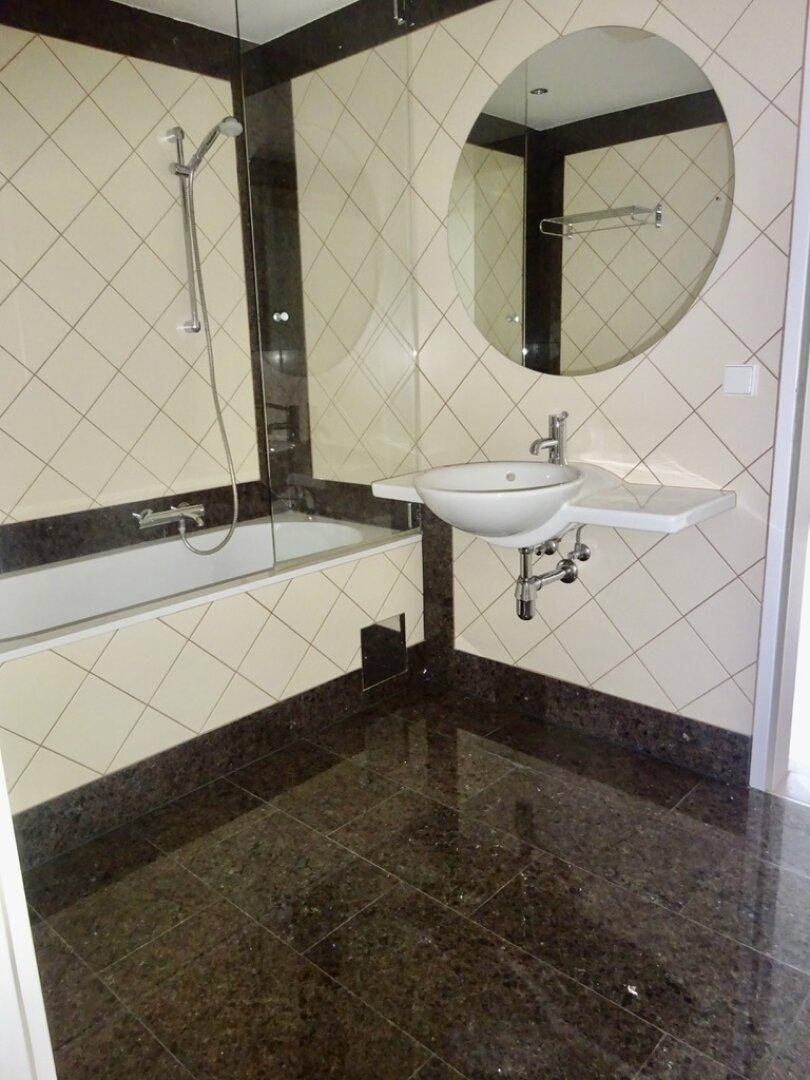 Modernes Badezimmer mit Badewanne, Waschbecken und dunklen Granitfliesen.