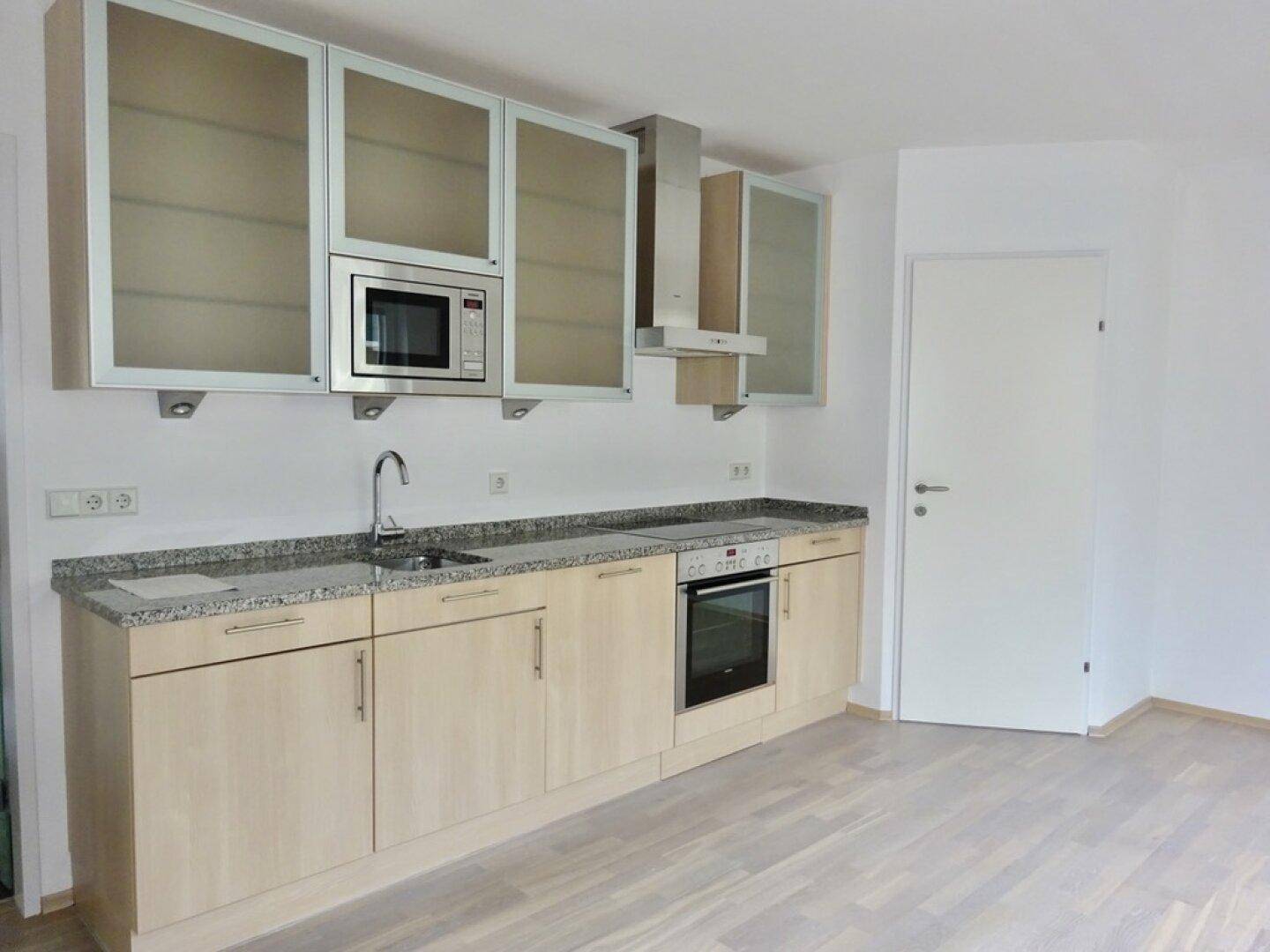 Moderne Einbauküche mit hellen Holzfronten, Granitarbeitsplatte und integrierten Geräten.