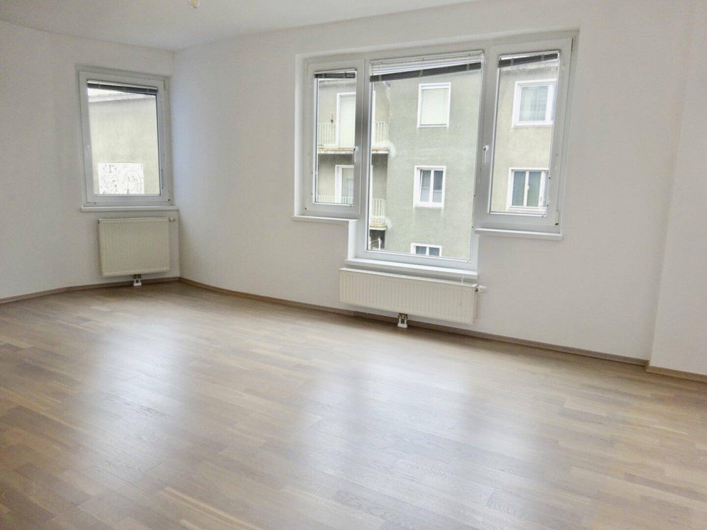Heller Raum mit Parkettboden und großen Fenstern, die viel Tageslicht hereinlassen.
