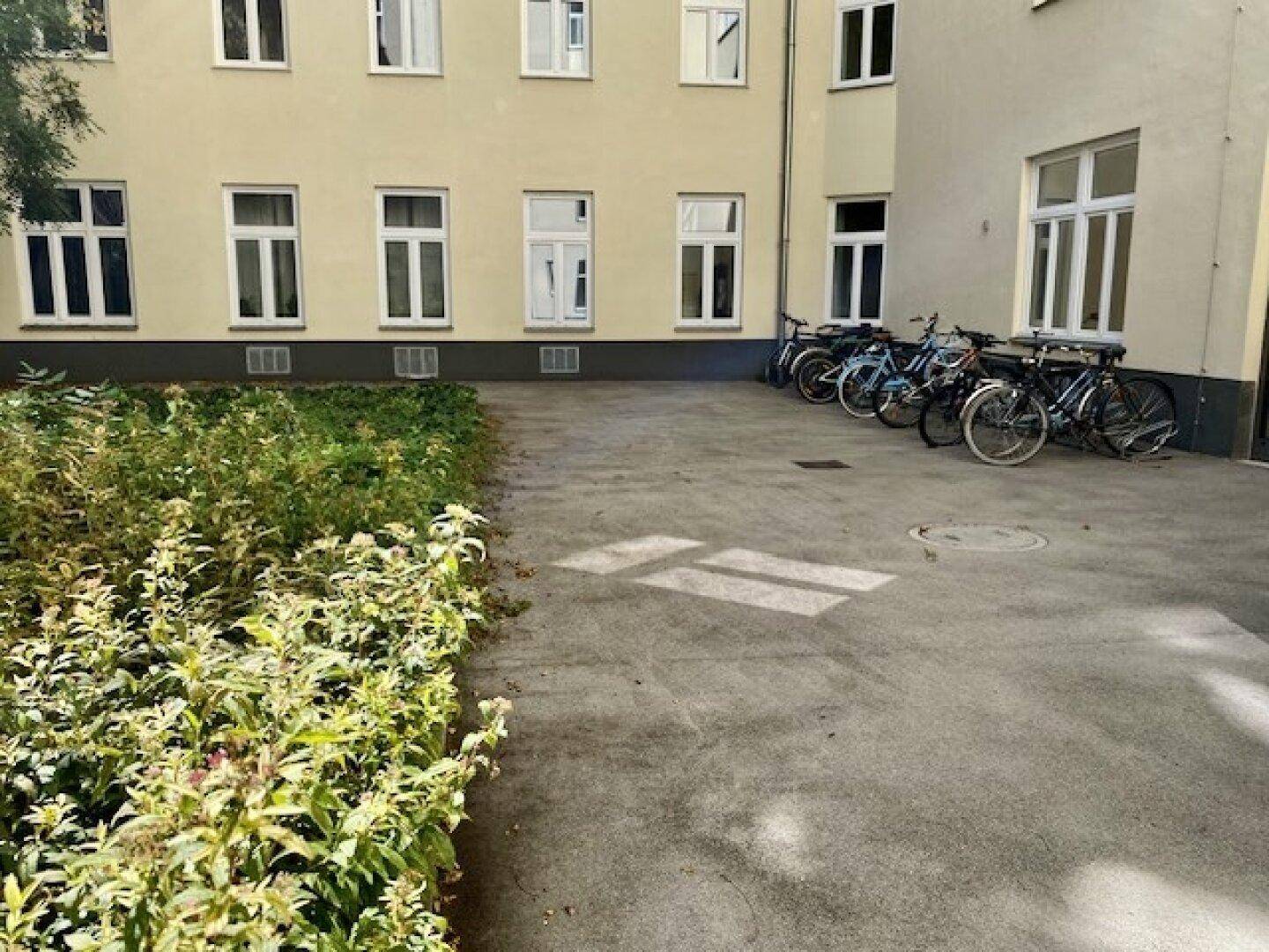 Grüner Innenhof eines Gebäudes mit Fahrradabstellplätzen und Bepflanzung.