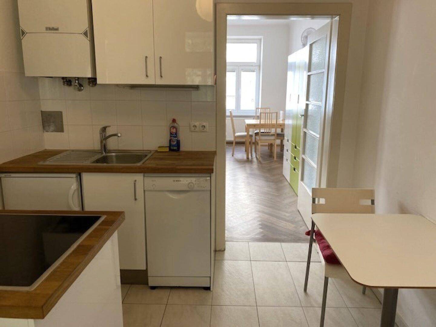 Küche mit Essbereich und Blick in den angrenzenden Wohn-Schlafbereich durch eine offene Tür.