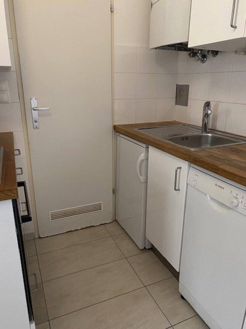 Küchenzeile mit Spüle, Geschirrspüler und kleinem Kühlschrank, daneben eine Tür.