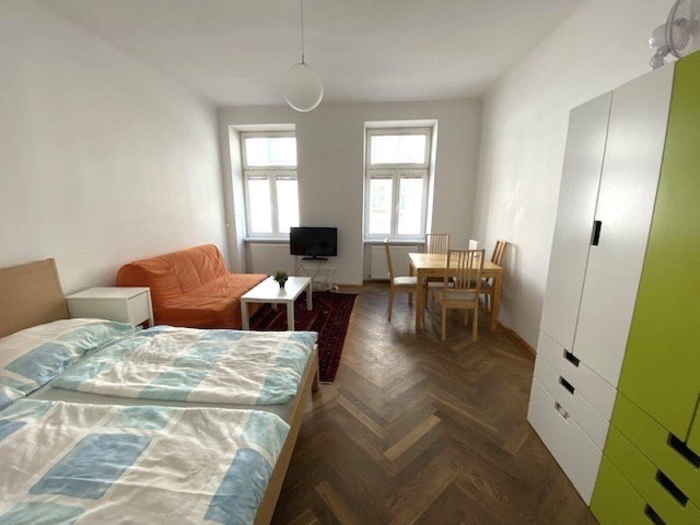 Kombinierter Wohn- und Schlafbereich mit Parkettboden, Esstisch und gemütlicher Sitzecke.