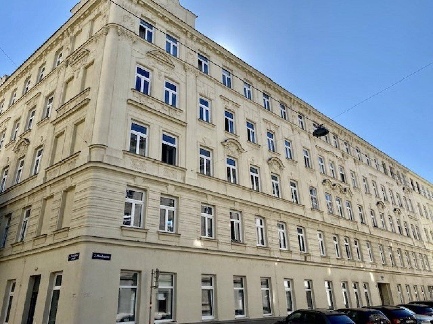 Historische Fassade eines Mehrfamilienhauses mit zahlreichen Fenstern unter blauem Himmel.