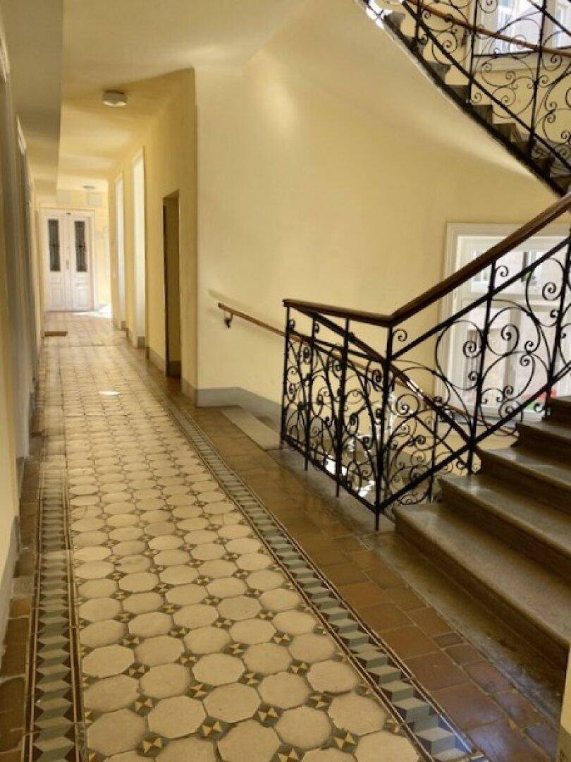 Historisches Treppenhaus mit kunstvollem Geländer und gemusterten Fliesen im Eingangsbereich.