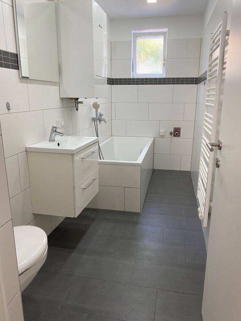 Modernes Badezimmer mit Badewanne, Waschbecken und beheiztem Handtuchhalter.
