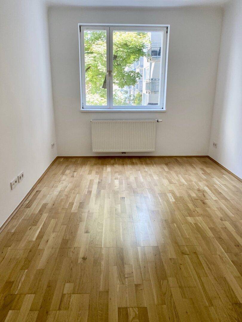Geräumiger Raum mit Parkettboden und großem Fenster mit Blick ins Grüne.