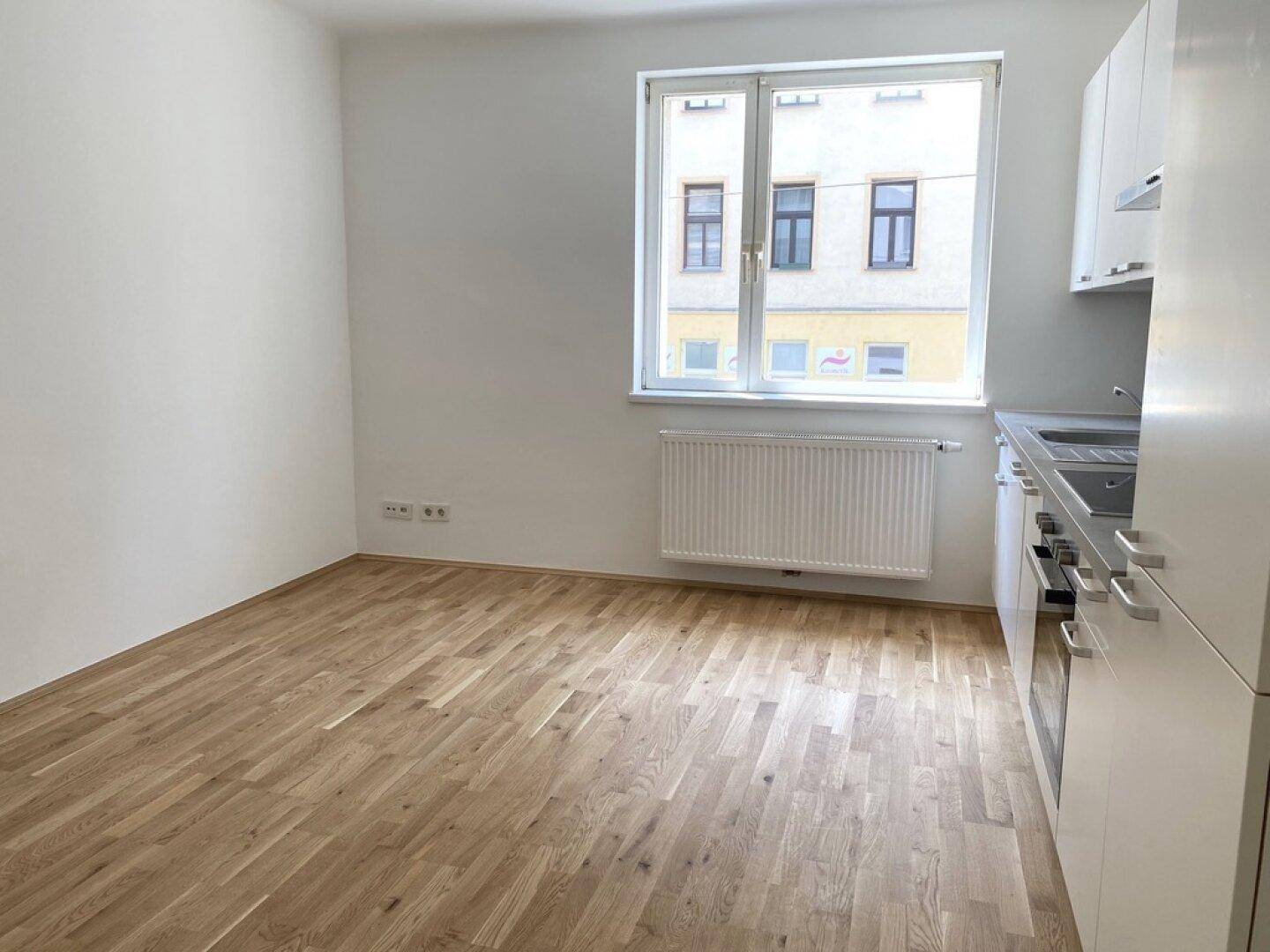 Offene Wohnküche mit weißer Einbauküche, Parkettboden und Blick auf die Straße.