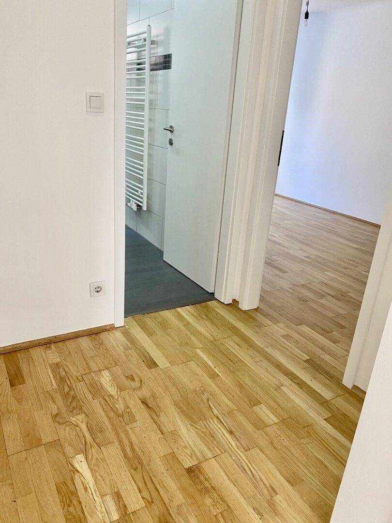 Heller Flur mit Parkettboden und Übergang zum gefliesten Badezimmer.