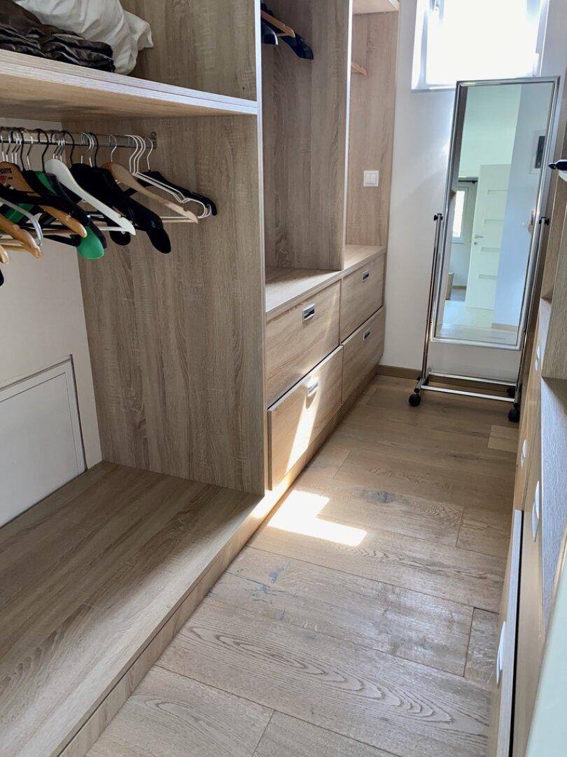 Begehbarer Kleiderschrank mit Holzregalen, Schubladen und einem großen Spiegel.