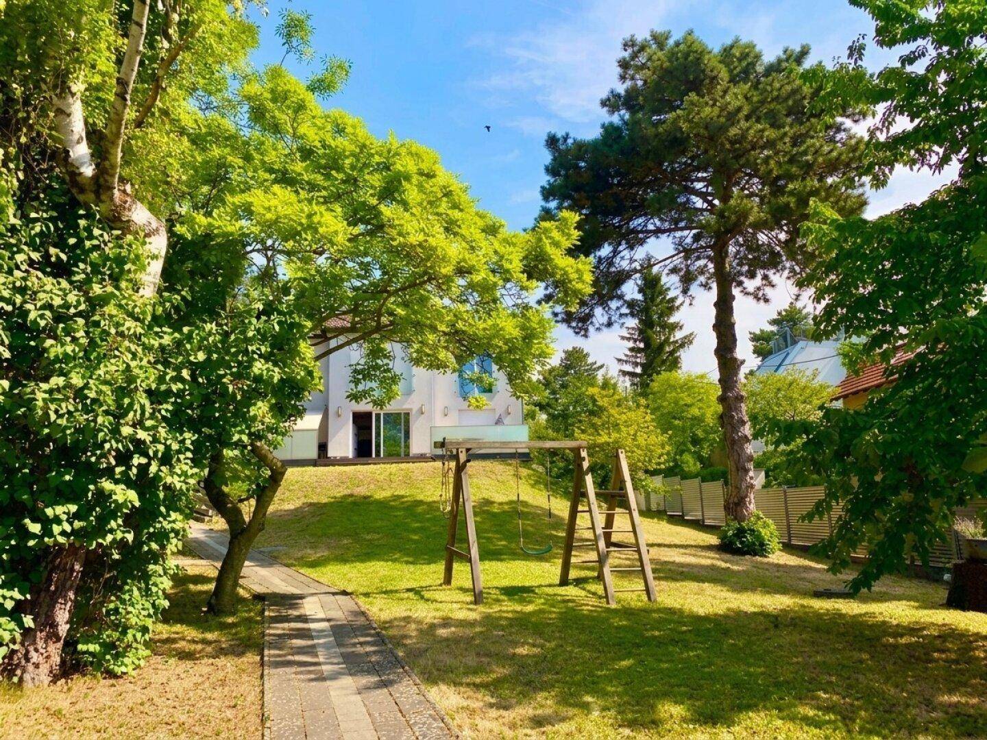 Großer grüner Garten mit Schaukel und altem Baumbestand, im Hintergrund das moderne Haus.
