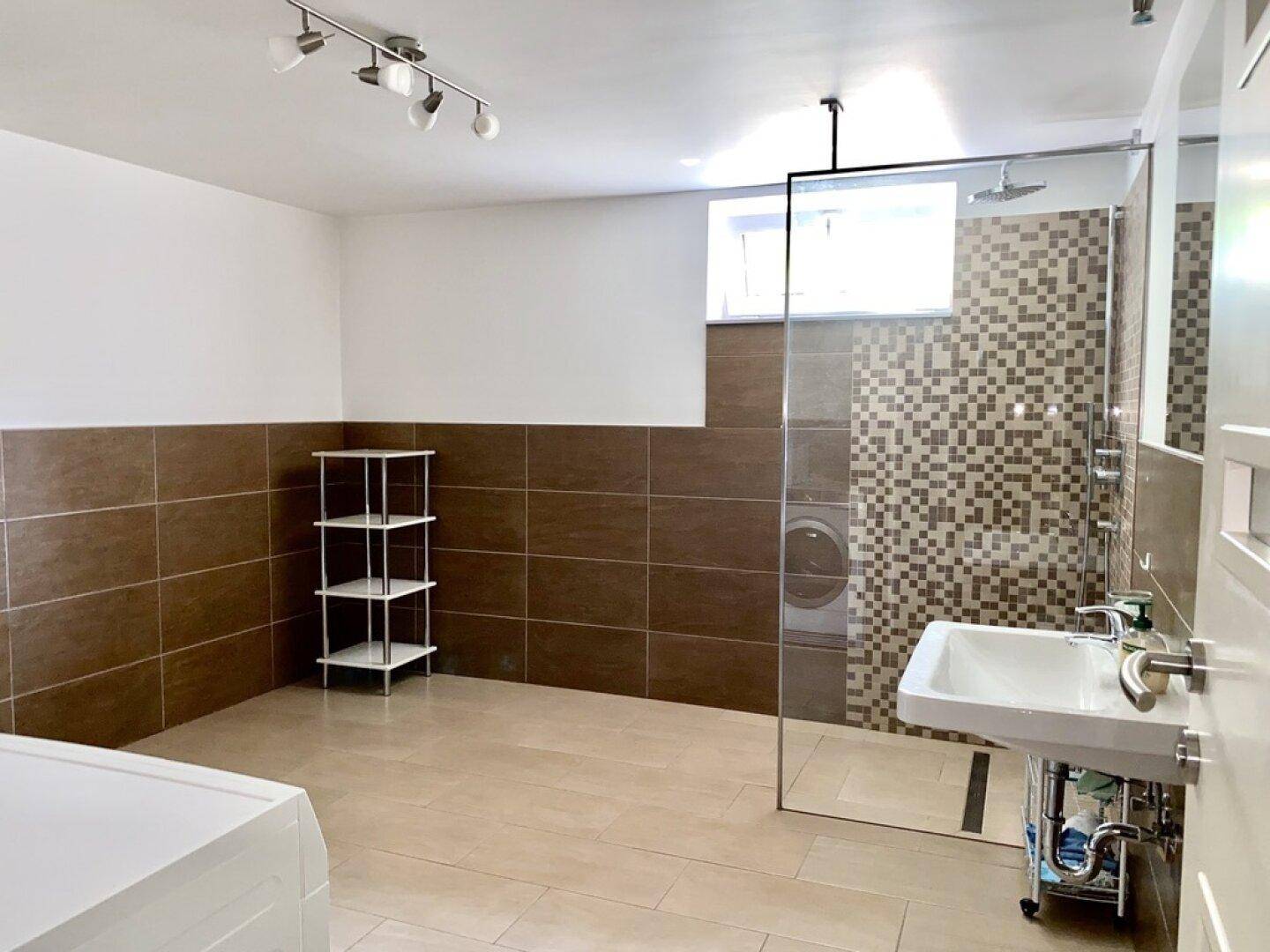 Modernes Badezimmer mit ebenerdiger Dusche, Waschbecken und braunen Fliesen.