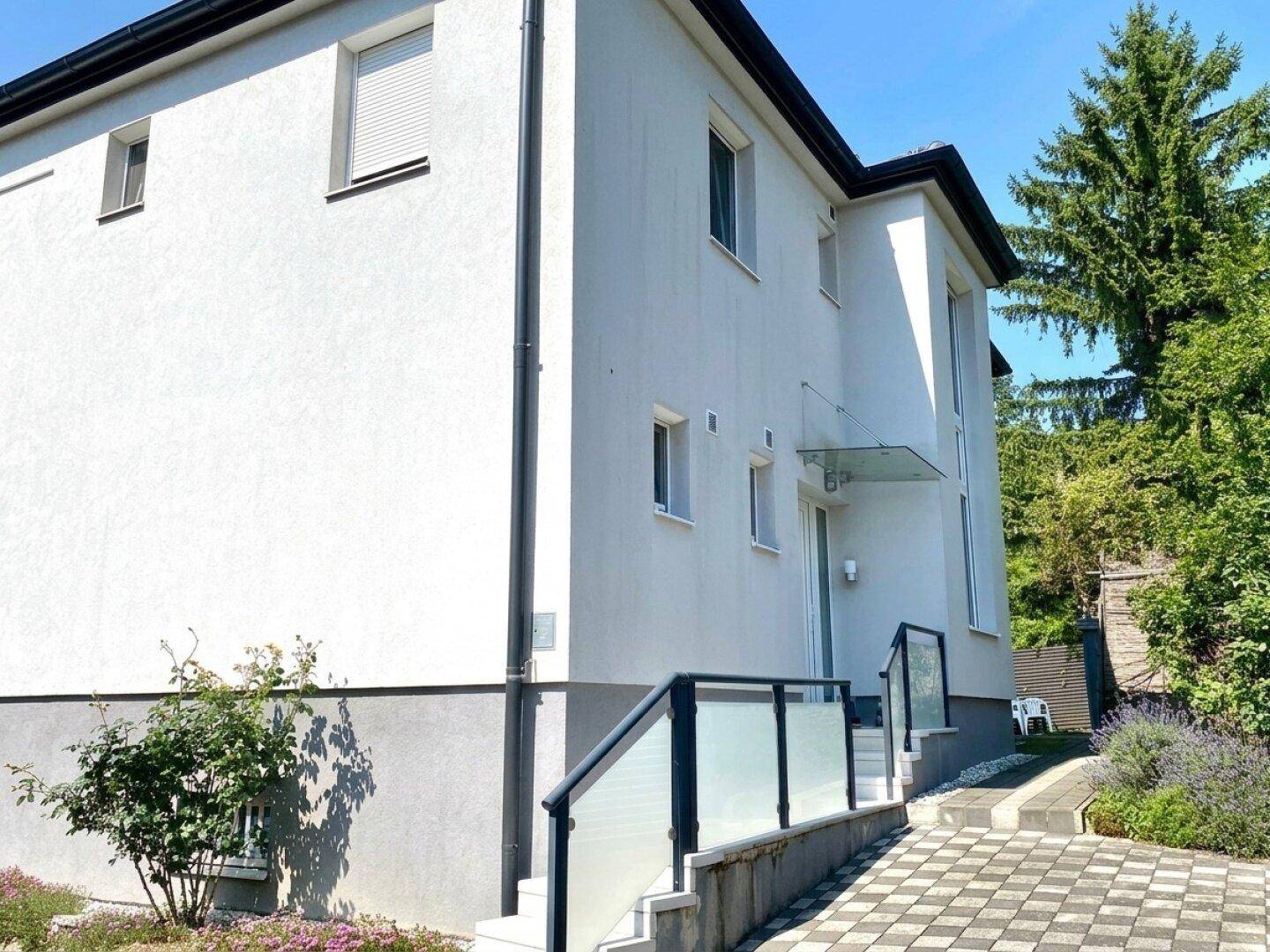 Seitenansicht des modernen Hauses mit Eingangsbereich und gepflastertem Zugang.