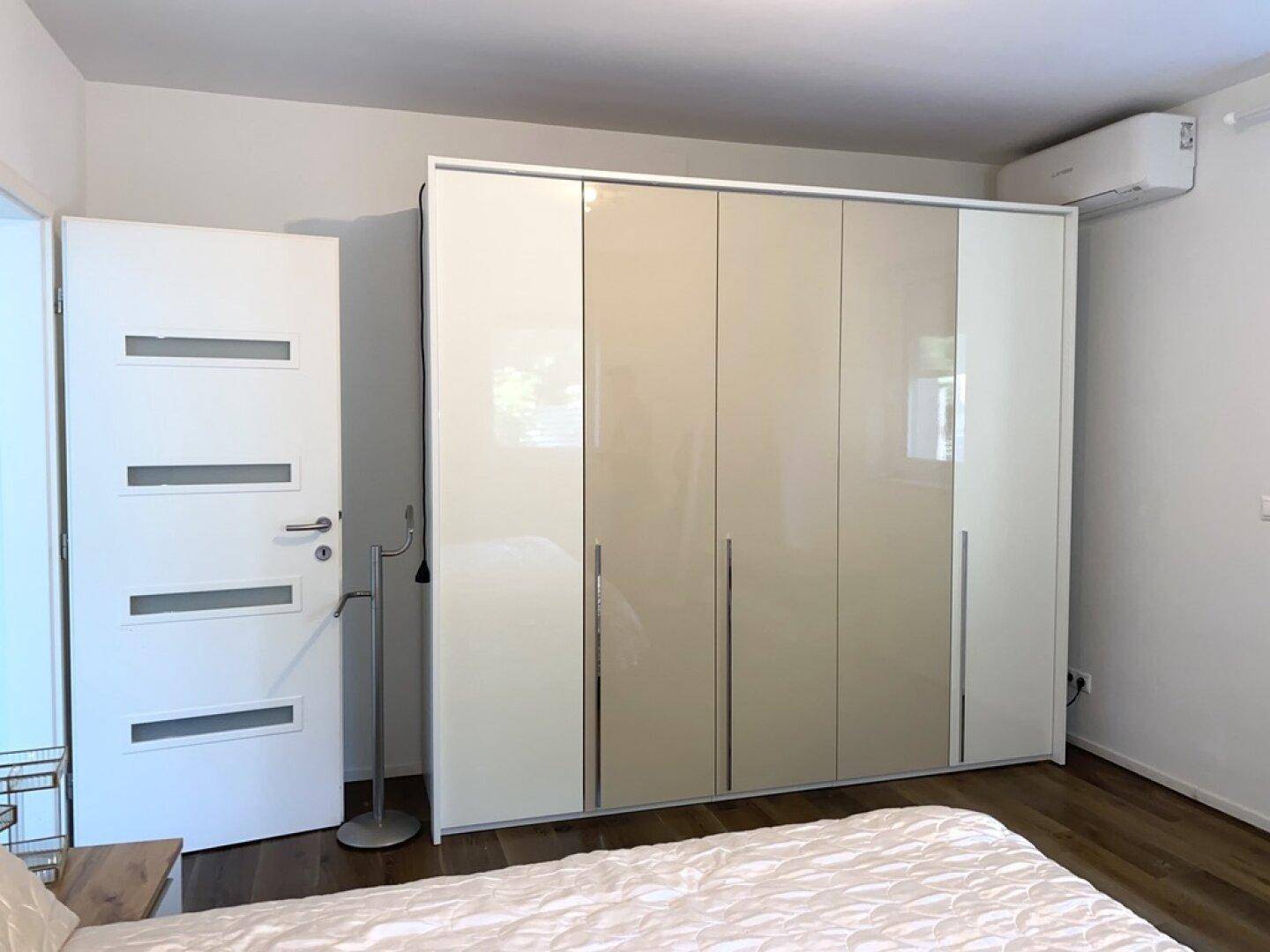 Schlafzimmer mit großem, modernem Kleiderschrank und Klimaanlage an der Wand.
