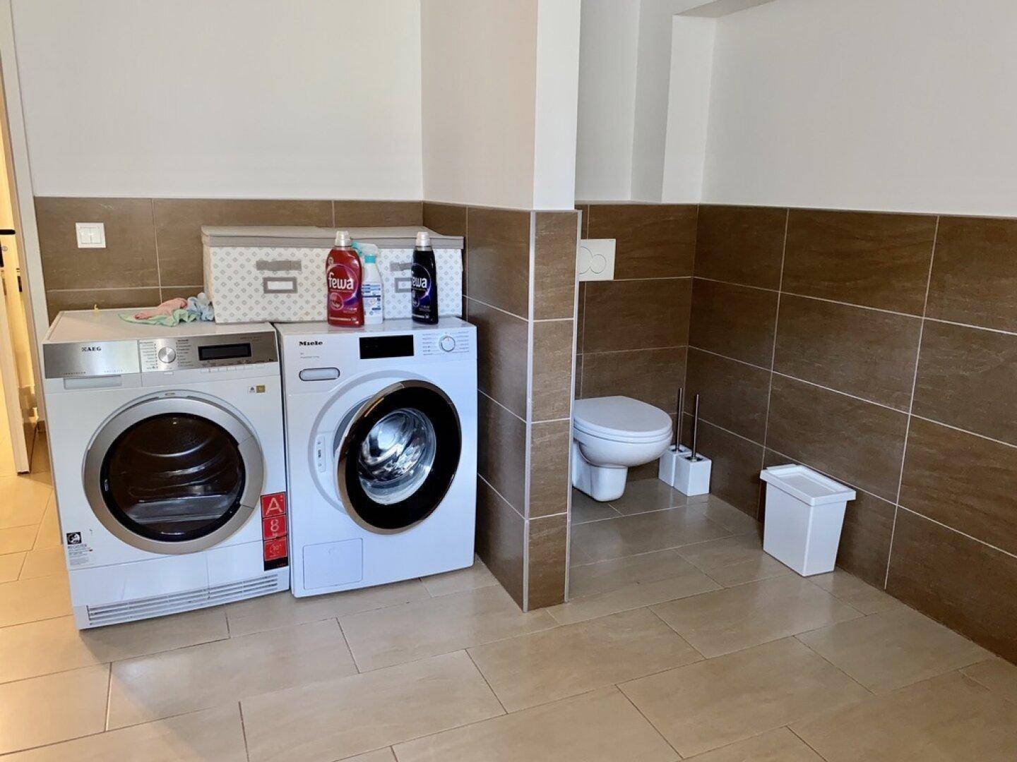 Praktischer Hauswirtschaftsraum mit Waschmaschine, Trockner und separatem WC-Bereich.