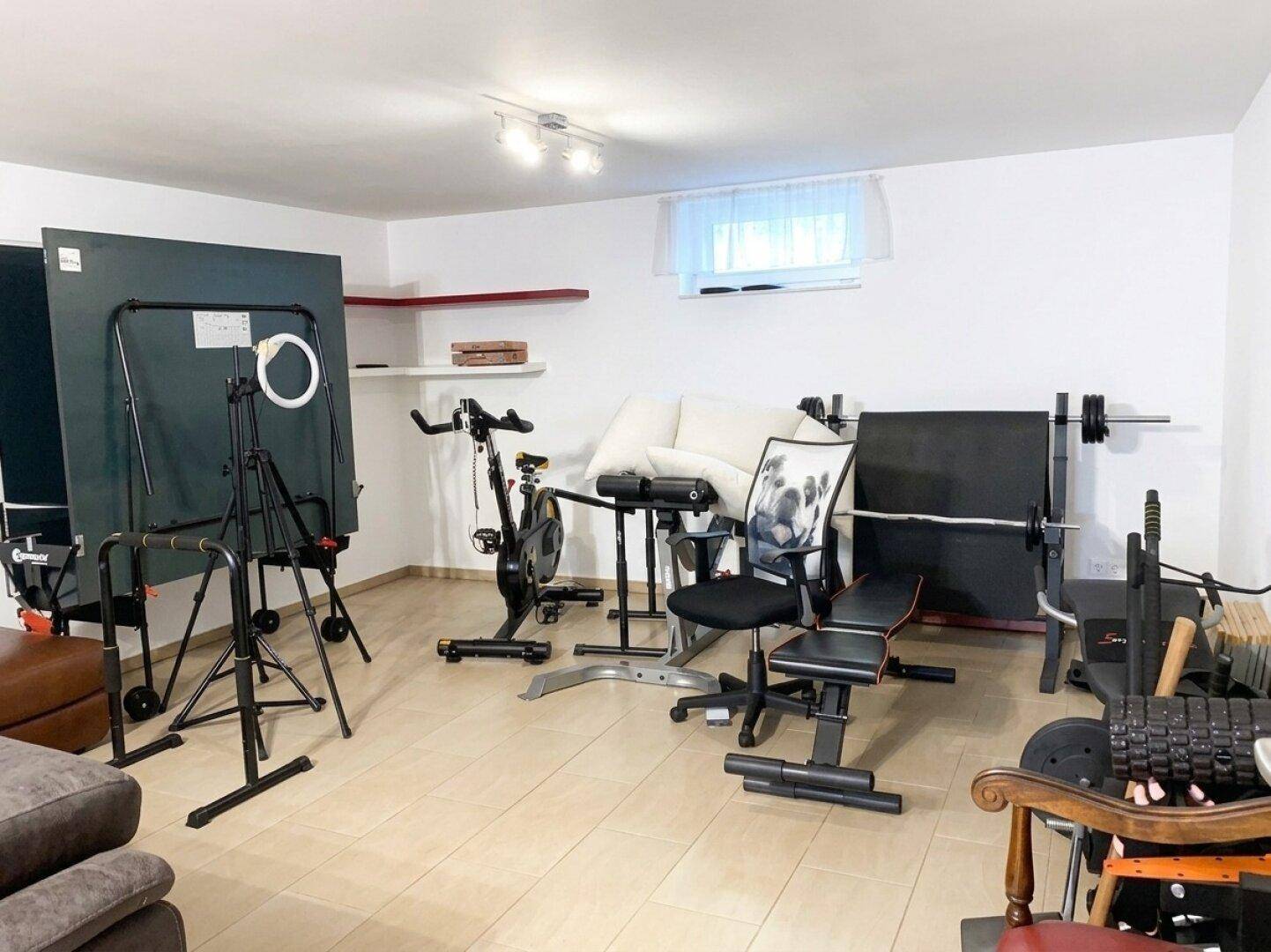 Geräumiger Fitnessraum im Untergeschoss mit verschiedenen Sportgeräten und Fliesenboden.