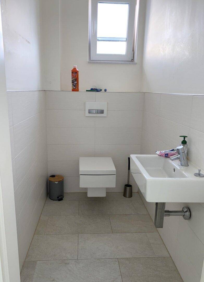 Modernes Gäste-WC mit wandhängender Toilette, Waschbecken und Fenster.