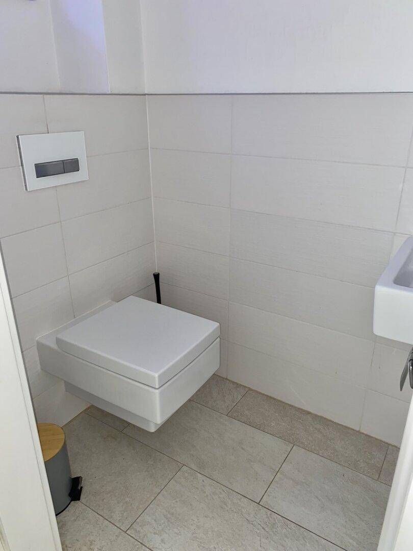 Helles Gäste-WC mit wandhängender Toilette, Waschbecken und weißen Fliesen.