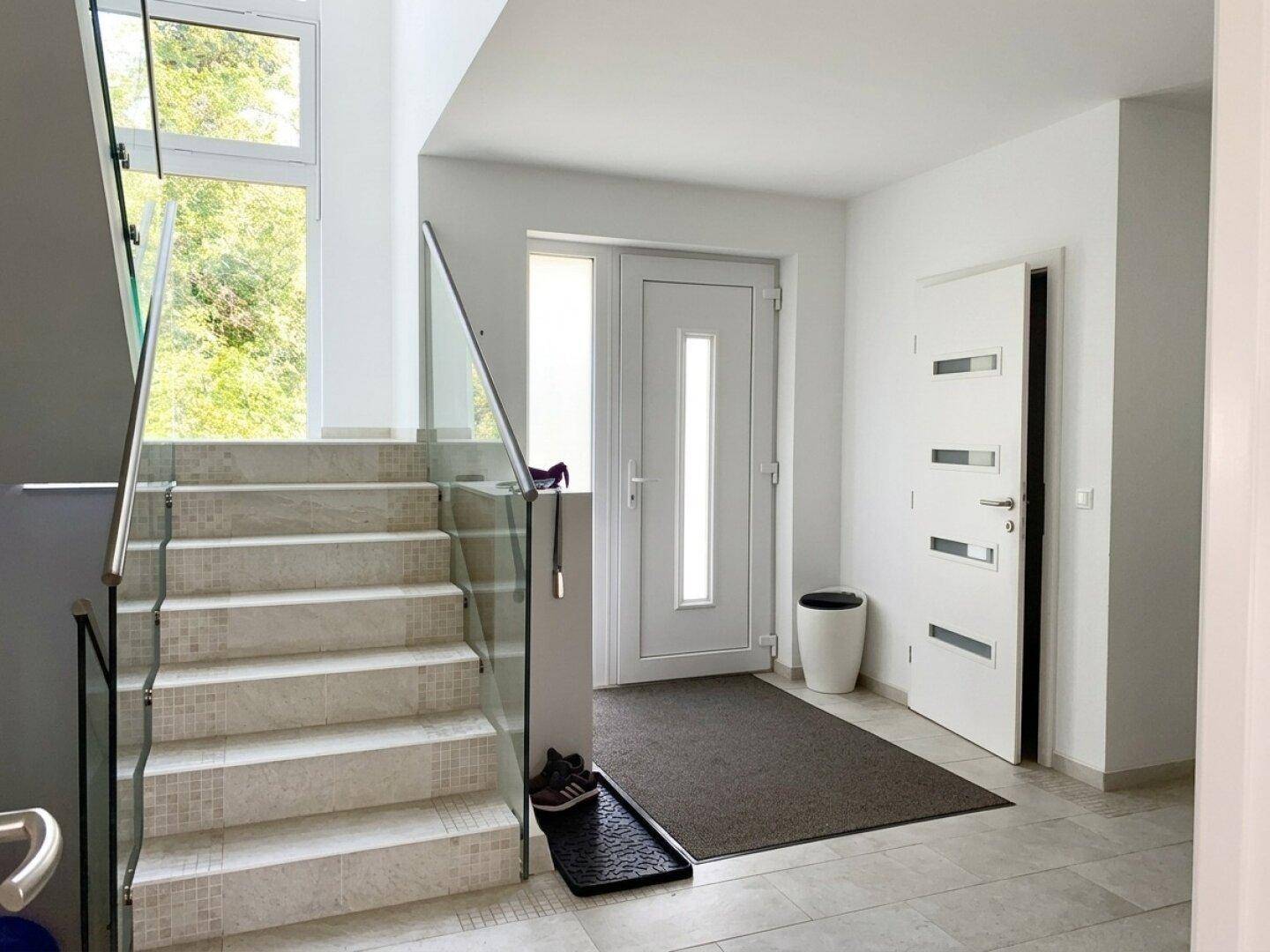 Heller Eingangsbereich mit moderner Treppe, Glasgeländer und Marmorstufen.