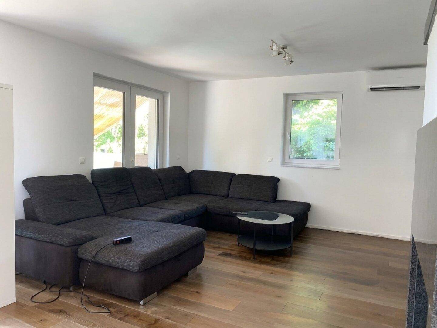 Gemütliches Wohnzimmer mit großem Ecksofa, Holzboden und Klimaanlage.
