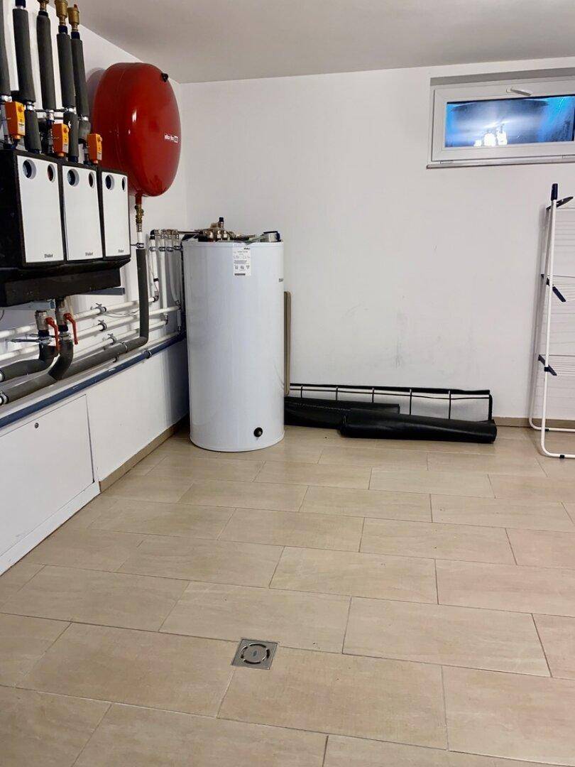 Hauswirtschaftsraum mit Warmwasserbereiter, Heizungsinstallationen und gefliestem Boden.