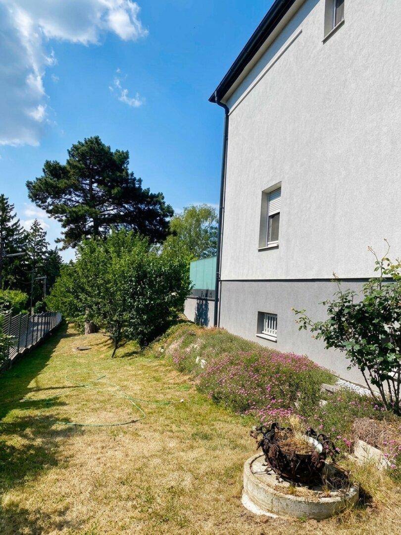 Seitenansicht des Hauses mit einem grünen Gartenbereich und blühenden Pflanzen.