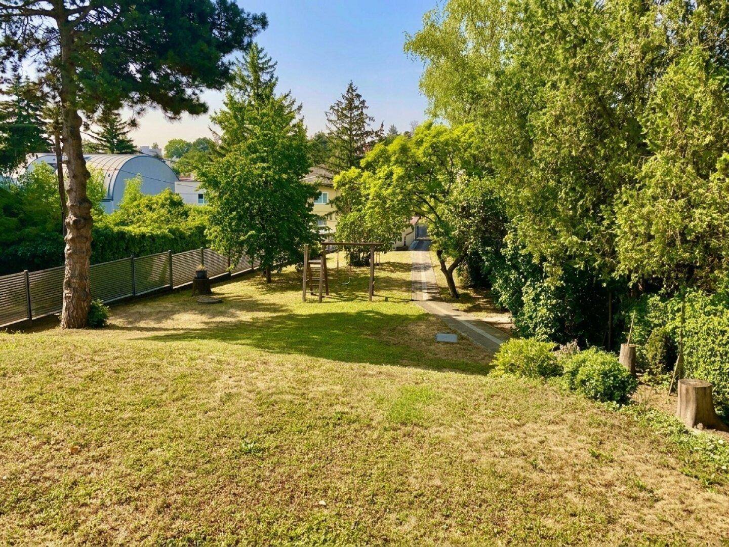 Großer Garten mit Rasenfläche, Bäumen und einem kleinen Spielplatz im Hintergrund.