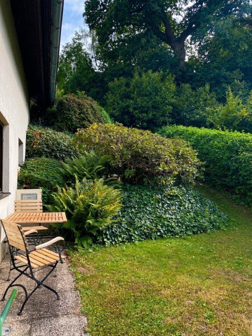 Gemütliche Terrasse mit Holztisch und Stühlen, umgeben von üppigem Grün und Pflanzen.