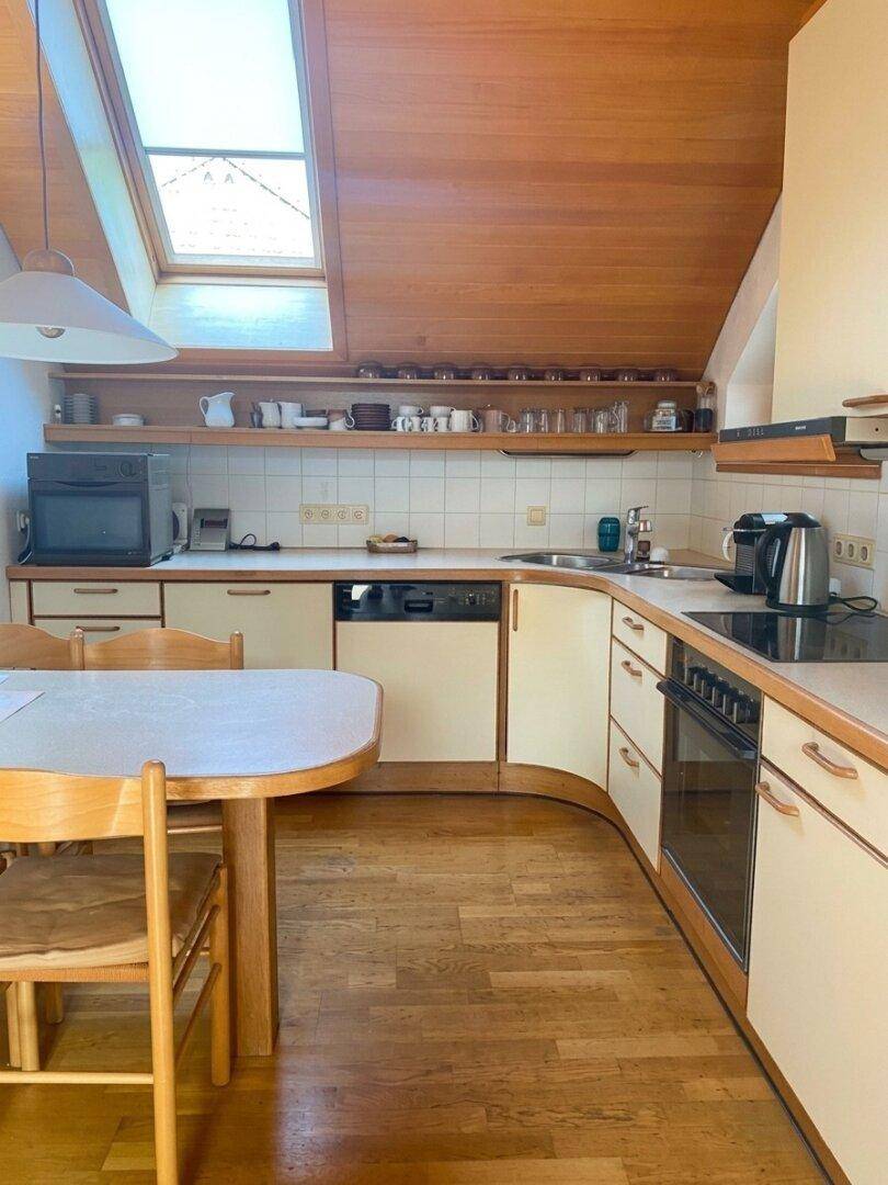 Gemütliche Küche mit Holzdachschräge, Einbauküche und einem kleinen Essbereich unter dem Dachfenster.