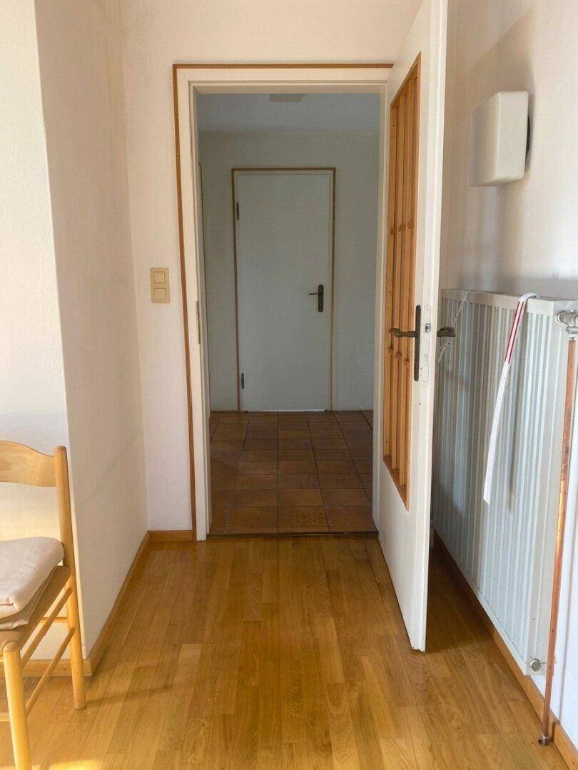 Heller Flur mit Holzboden und weiß gestrichenen Wänden, der zu weiteren Räumen führt.