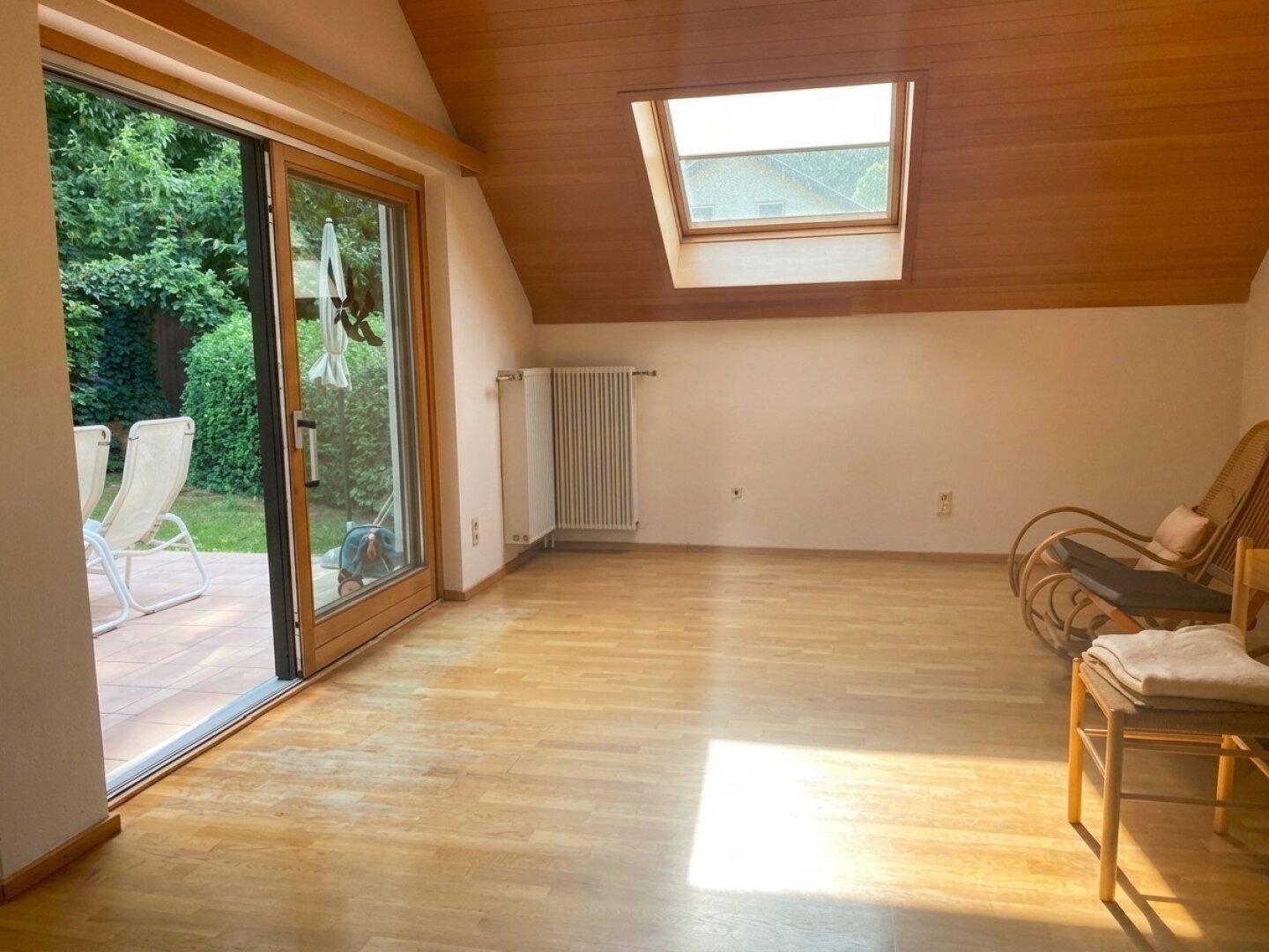 Heller Wohnraum mit Holzboden, Zugang zur Terrasse und Dachschräge mit einem Dachfenster.