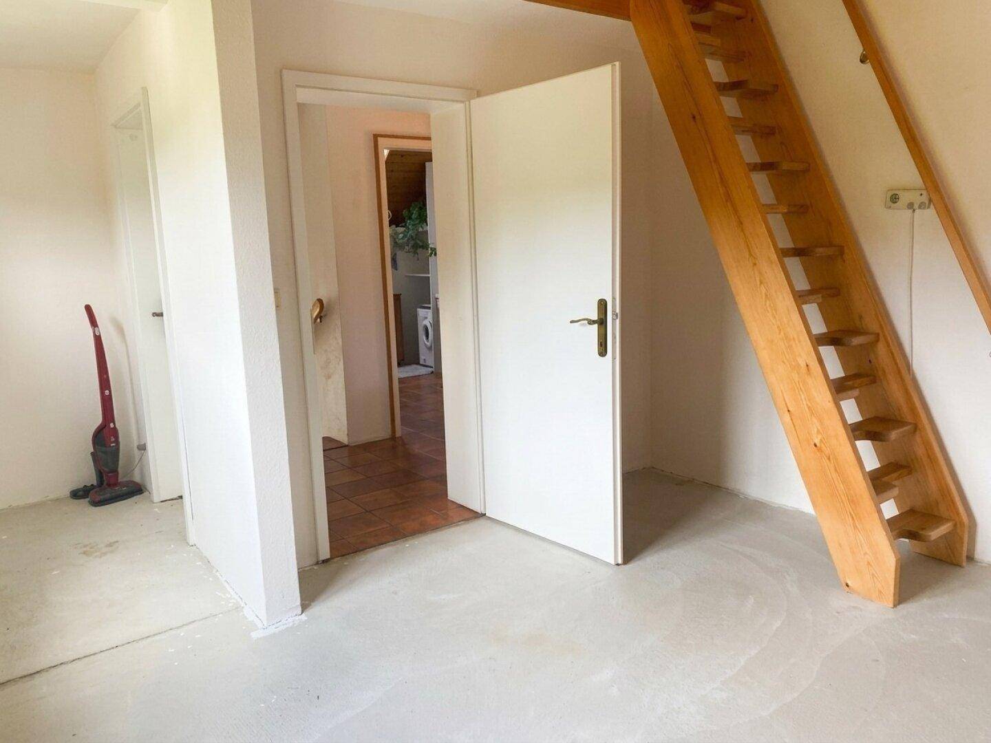Geräumiger Raum mit Betonboden und Holztreppe, die zu einer oberen Galerie führt.
