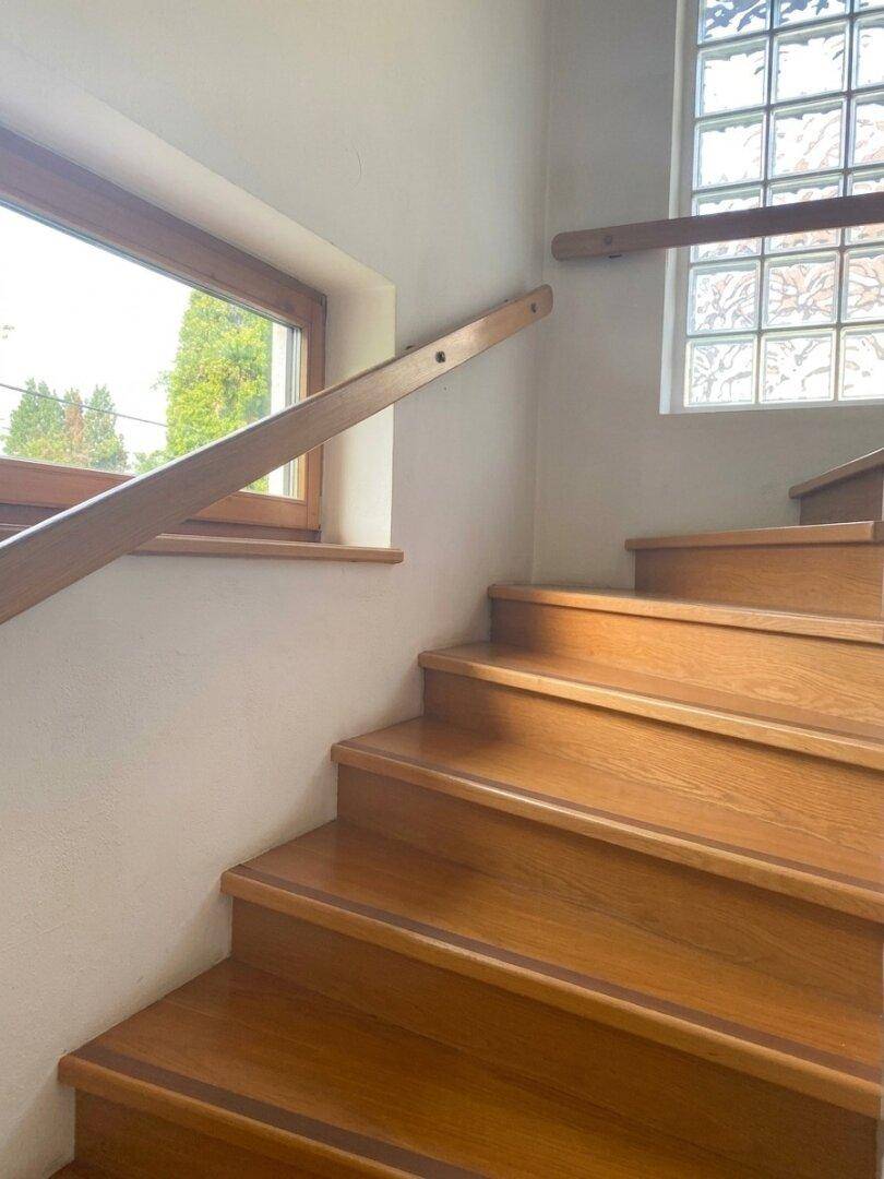Helle Holztreppe mit Holzgeländer und einem Fenster, das Tageslicht hereinlässt.