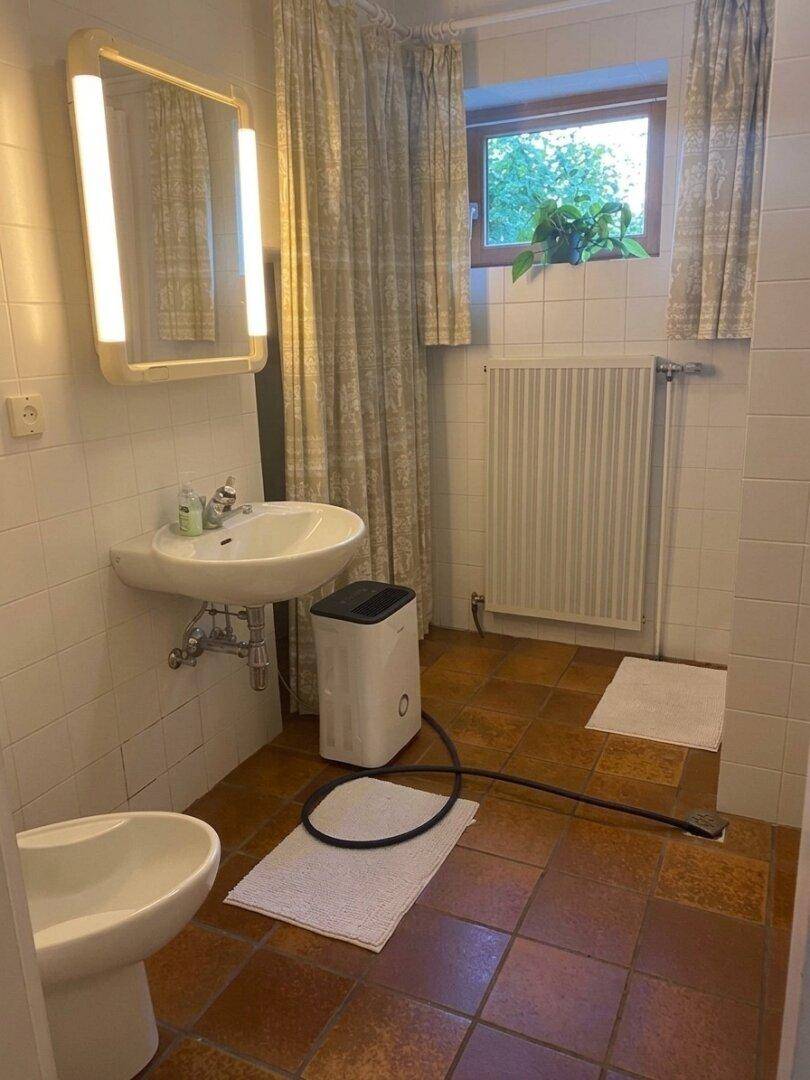 Badezimmer mit weißen Fliesen, Terrakotta-Boden, Waschbecken und einem Fenster.