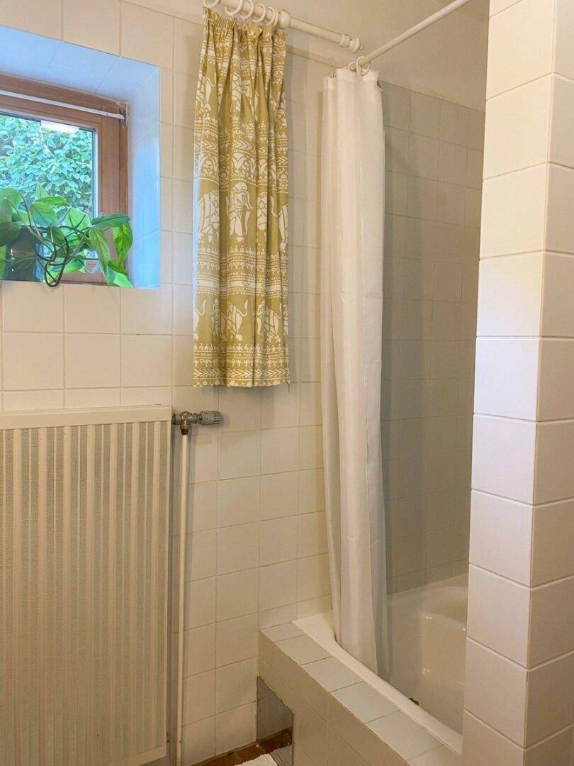 Badezimmer mit Duschvorhang über einer Badewanne und einem Fenster mit Blick ins Grüne.
