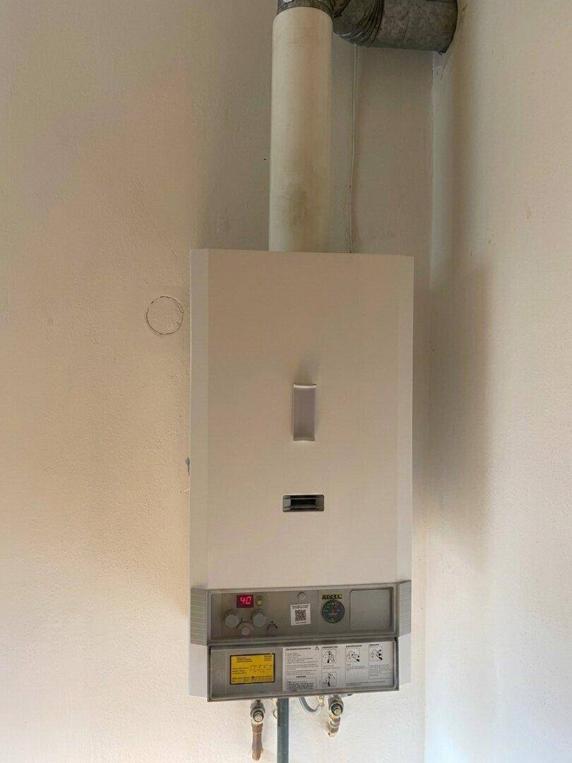 Wandmontierter Warmwasserbereiter mit digitaler Anzeige in einem einfachen Raum.