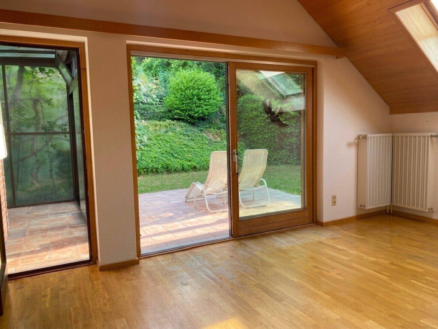 Helles Wohnzimmer mit Holzboden, Zugang zur Terrasse und einem angrenzenden Wintergarten.