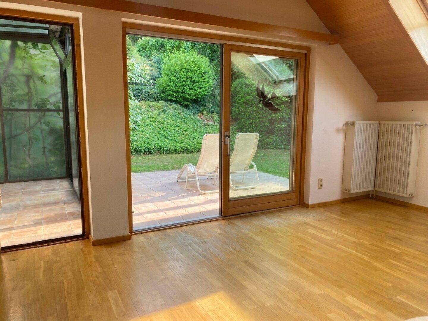 Heller Wohnraum mit Holzboden, Zugang zur Terrasse und Blick in den grünen Garten.