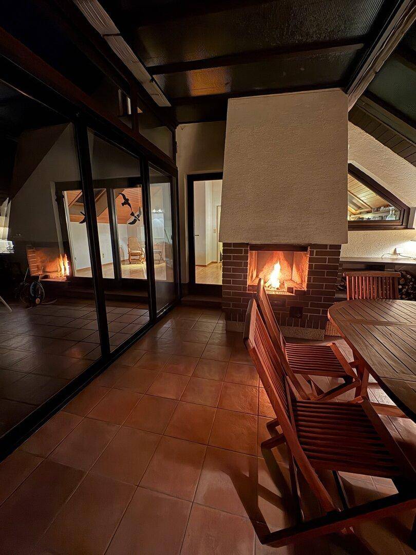 Stimmungsvoller Wintergarten am Abend mit brennendem Kamin und gemütlicher Beleuchtung.