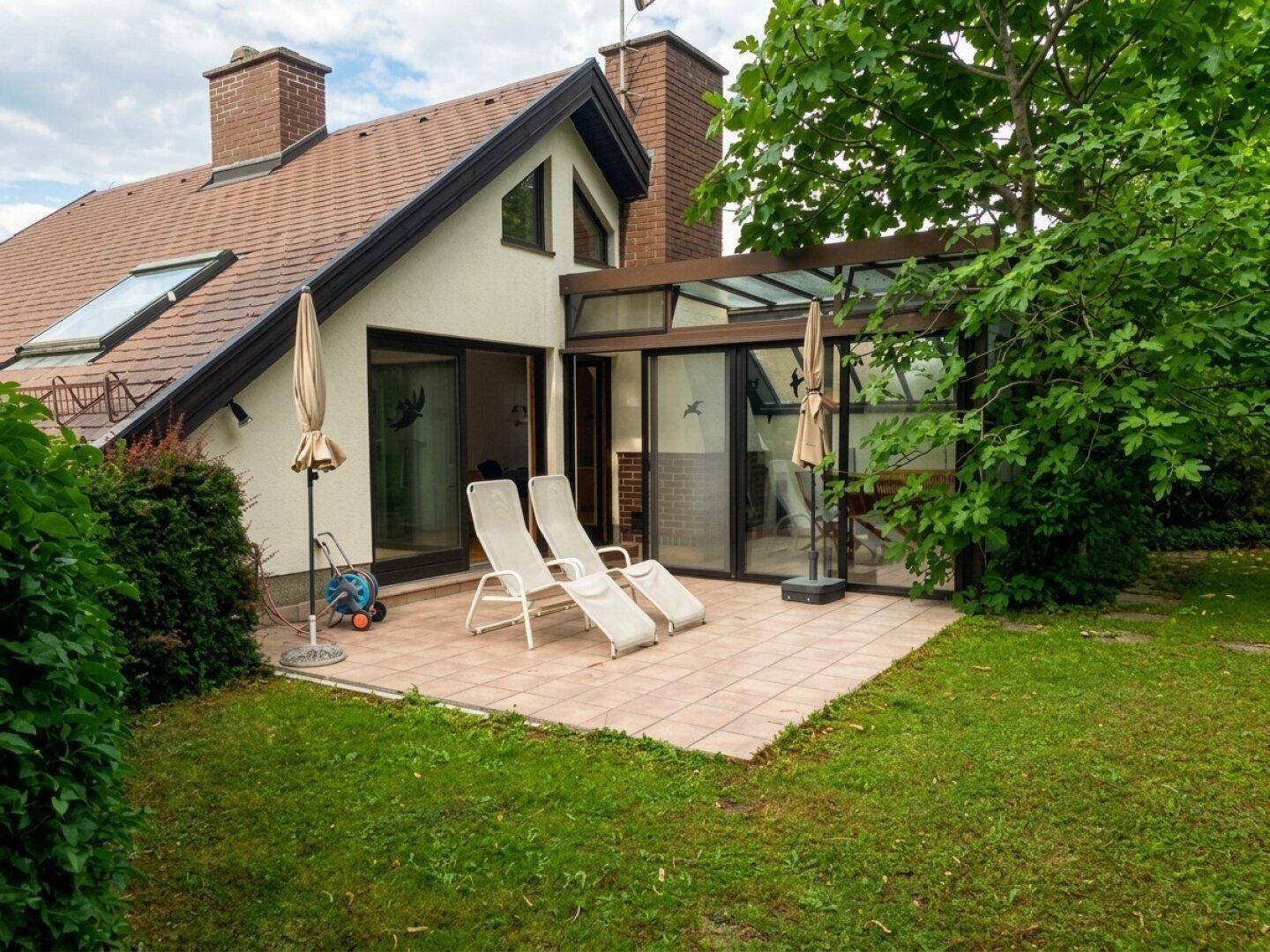 Geräumige Terrasse mit Liegestühlen und Blick auf den grünen Garten und Wintergarten.