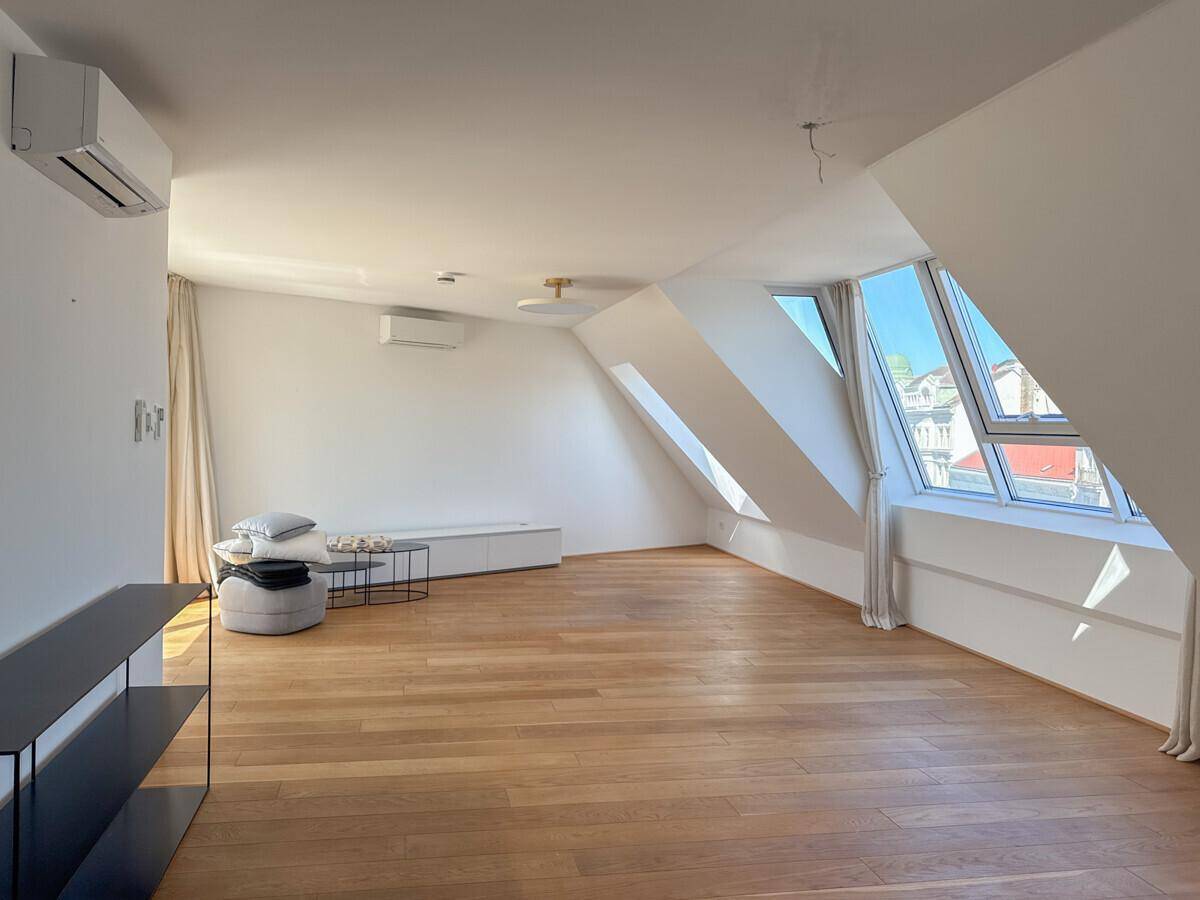 Helles Wohnzimmer im Dachgeschoss mit schrägen Decken, großen Fenstern und Holzboden.
