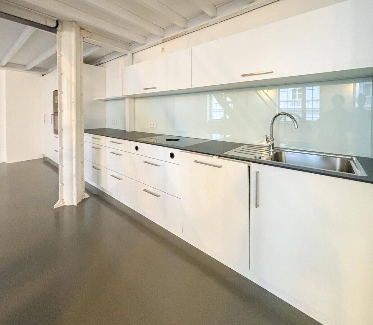 Moderne Einbauküche mit weißen Schränken, dunkler Arbeitsplatte und integrierter Spüle.