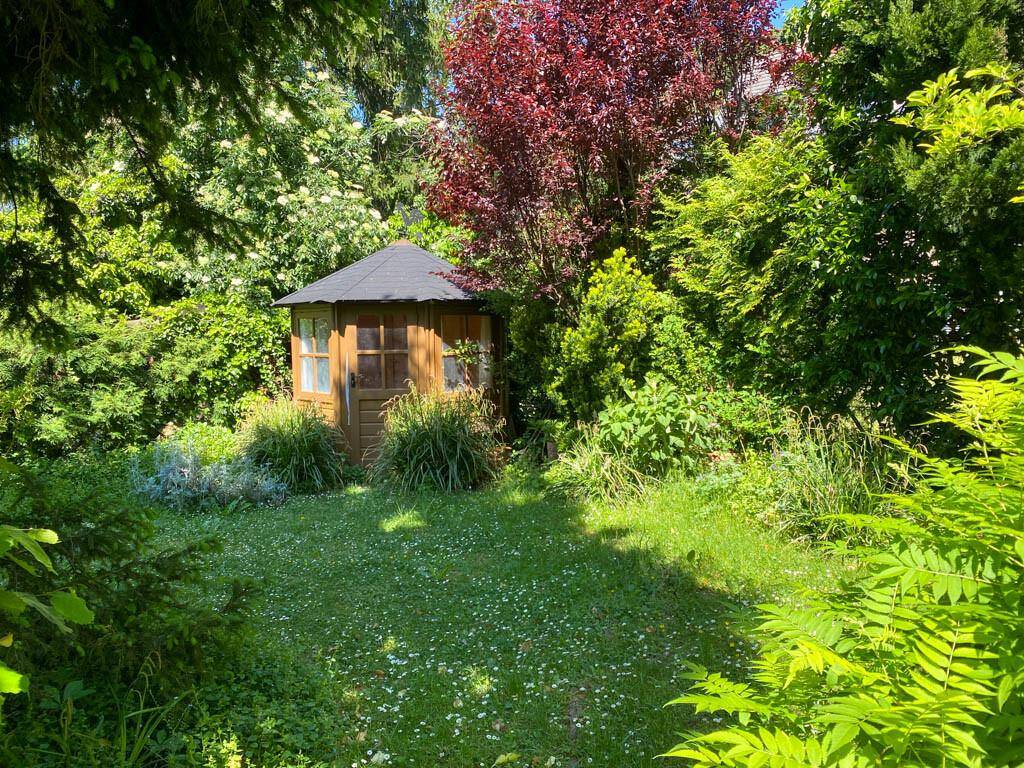 Idyllischer Garten mit einem charmanten Holzpavillon, umgeben von dichtem Grün und Bäumen.