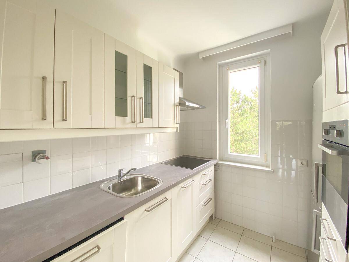 Funktionale Küche mit weißen Einbauschränken, Spüle und Fenster mit Blick ins Grüne.