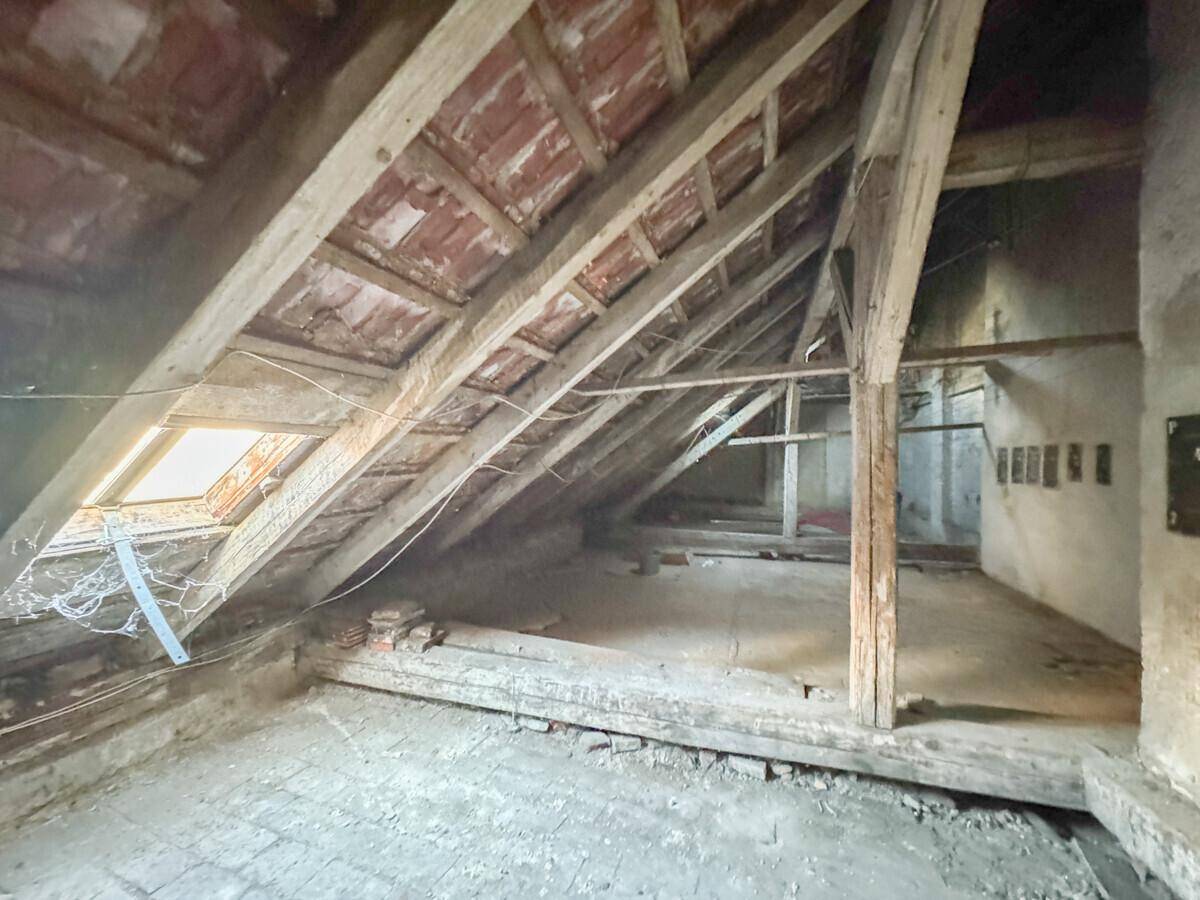Unausgebauter Dachboden mit sichtbaren Holzbalken und einem Dachfenster, viel Potenzial.