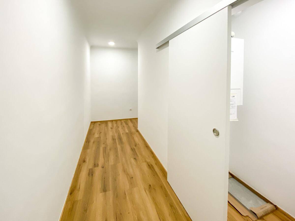 Heller Flur mit Laminatboden, weißen Wänden und praktischer Schiebetür.