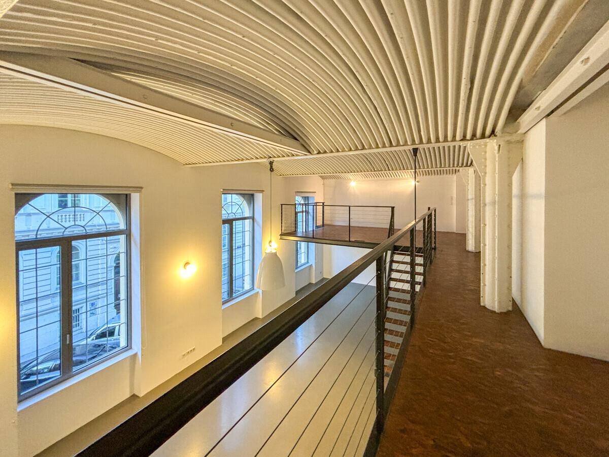 Blick von der Galerie auf den unteren Wohnbereich mit großen Fenstern und hoher Decke.