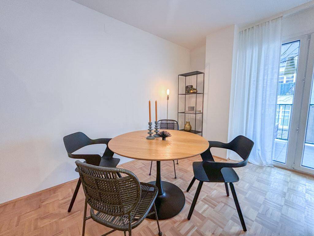 Heller Essbereich mit modernem Holztisch, schwarzen Stühlen und Balkonzugang.