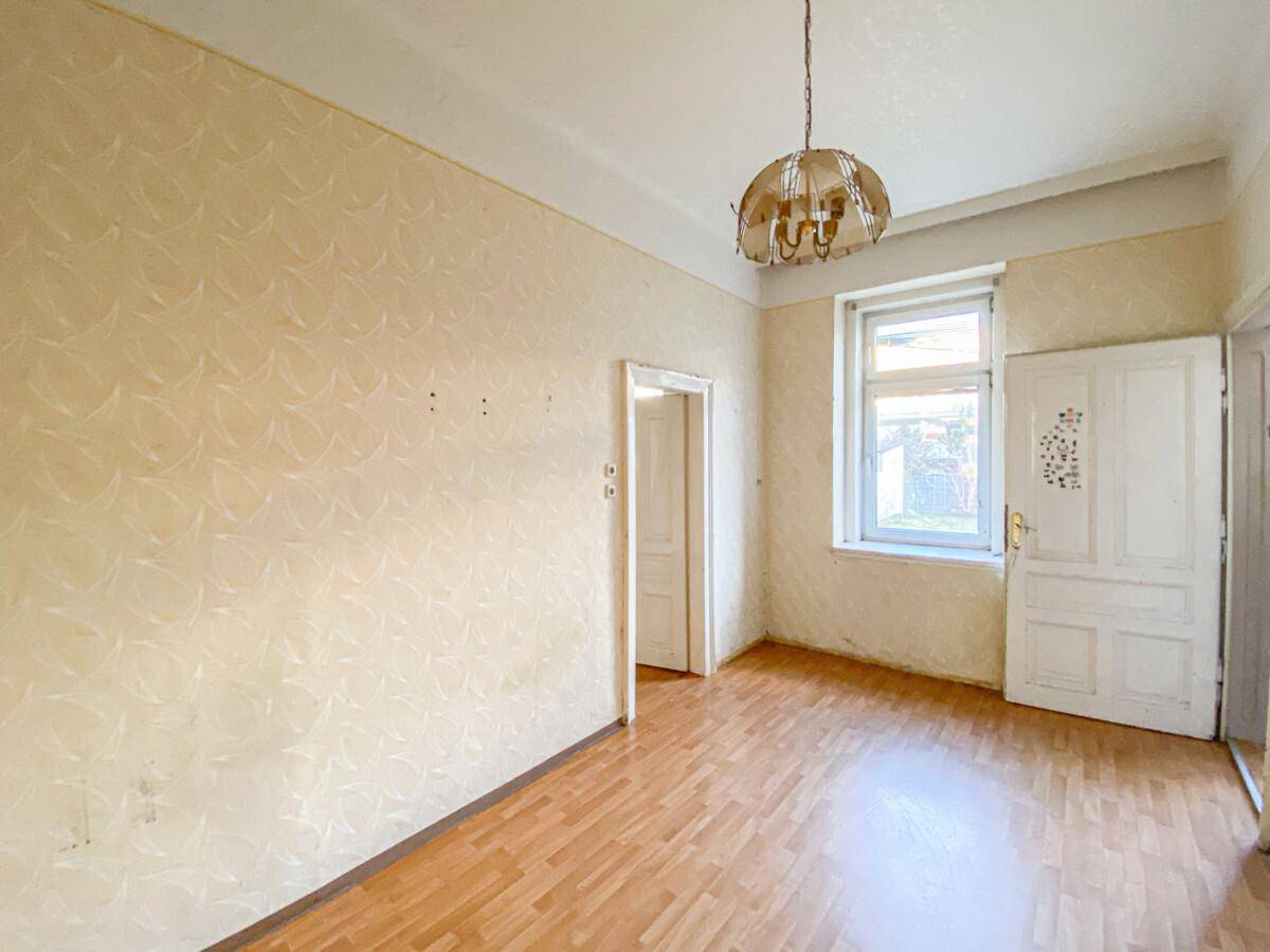 Lichtdurchfluteter Raum mit Parkettboden, einem Fenster und einer klassischen Deckenleuchte.